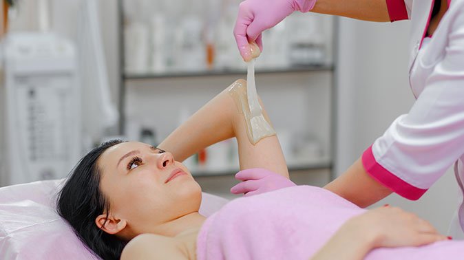 professional woman making wax another woman arm